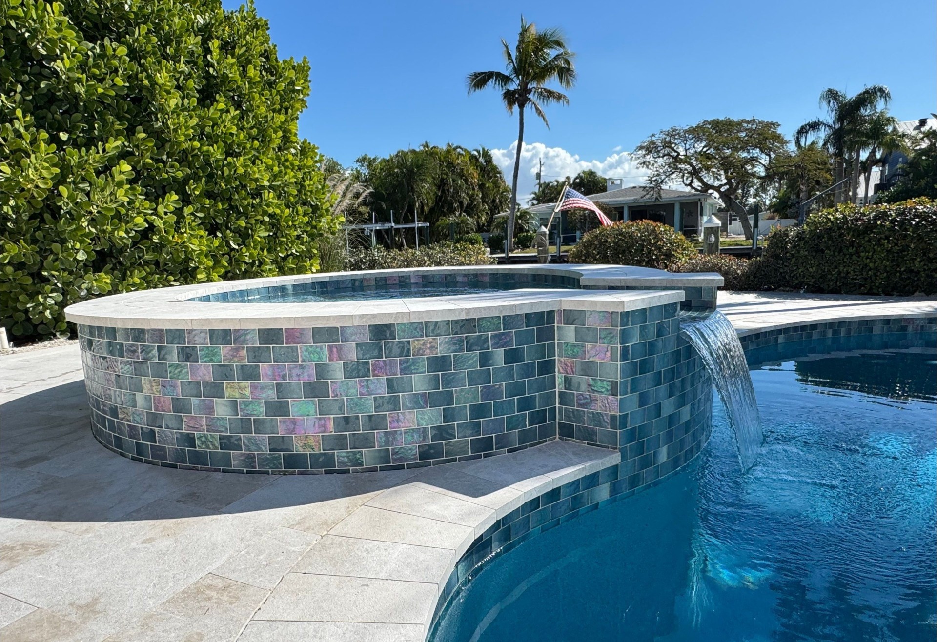 Renovated spa with iridescent glass tile and travertine coping by Nelson Pool Company